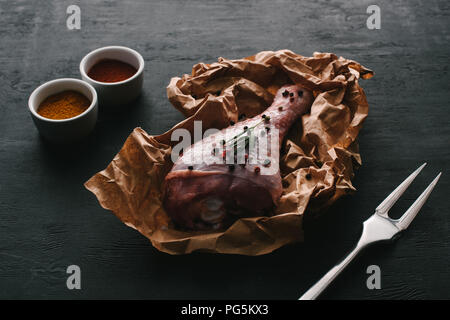 raw turkey leg with pepper corns on baking paper on wooden table with paprika spices Stock Photo