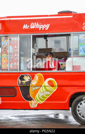 Glum looking female ice cream vendor, seller on a rainy day. No customers. Ice cream van. Mr Whippy. No sales. Bored. Wet day. Dejected Stock Photo