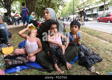 August 14, 2018 - Paris, France: A Syrian family sit in a public park near porte d'Aubervilliers as they wait for a charity to find them emergency shelter for the night. The family of eight members, two parents and six children, come from the province of Idlib and has been seeking asylum in France for several months as they struggle with the French bureaucracy rules. The 34 year-old mother, Kiraz Hamza, is pictured with her twin daughters Fatima and Amna, aged 3 and half year old, and her 6 year-old son Youssef. Portrait dÕune famille de migrants syriens ˆ la rue depuis leur arrivee a Paris, i Stock Photo