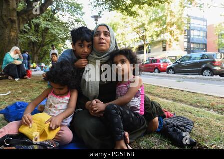 August 14, 2018 - Paris, France: A Syrian family sit in a public park near porte d'Aubervilliers as they wait for a charity to find them emergency shelter for the night. The family of eight members, two parents and six children, come from the province of Idlib and has been seeking asylum in France for several months as they struggle with the French bureaucracy rules. The 34 year-old mother, Kiraz Hamza, is pictured with her twin daughters Fatima and Amna, aged 3 and half year old, and her 6 year-old son Youssef. Portrait dÕune famille de migrants syriens ˆ la rue depuis leur arrivee a Paris, i Stock Photo