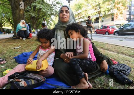 August 14, 2018 - Paris, France: A Syrian family sit in a public park near porte d'Aubervilliers as they wait for a charity to find them emergency shelter for the night. The family of eight members, two parents and six children, come from the province of Idlib and has been seeking asylum in France for several months as they struggle with the French bureaucracy rules. The 34 year-old mother, Kiraz Hamza, is pictured with her twin daughters Fatima and Amna, aged 3 and half year old. Portrait dÕune famille de migrants syriens ˆ la rue depuis leur arrivee a Paris, il y a pres de huit mois. Ils pas Stock Photo