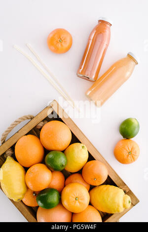 top view of various citrus fruits in wooden box with bottles of juice on white surface Stock Photo