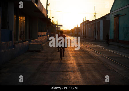 Back view of a Cuban man cycling along a disused railway track up a street into the setting sun in Cienfuegos Cuba Stock Photo