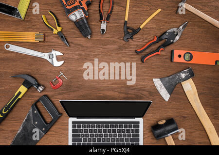 top view of laptop with blank screen surrounded by arranged various tools on wooden table Stock Photo