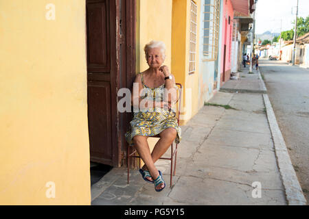 Elderly Spanish/Cuban woman sitting on a chair outside her house in the evening in Trinidad Cuba Stock Photo