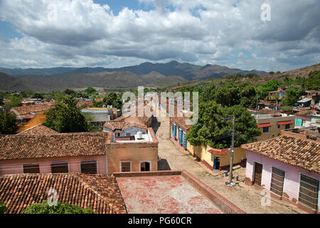 A view of the terracotta roofs and street houses of Trinidad Cuba from above with cloudy skies above the mountains in the background Stock Photo
