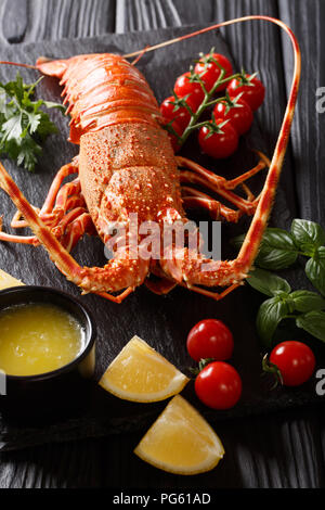 Expensive food: spiny boiled lobster with fresh tomato, lemon and melted butter close-up on black stone. vertical Stock Photo