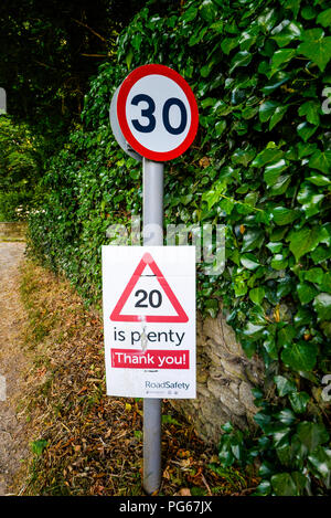 20 is plenty thank you. Temporary, unofficial speed limit placard attached to official 30 mph road speed sign. Quiet English village lane with trees Stock Photo