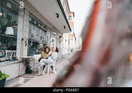 Two laughing friends sitting in front of coworking space Stock Photo