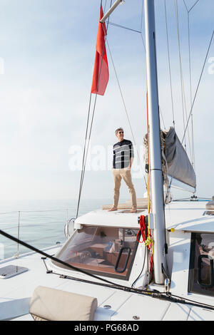 Mature man standing on a catamaran with hands in pockets, smiling Stock Photo