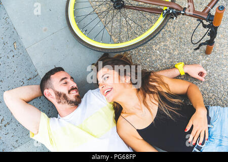 Happy couple lying on the ground next to bicycle and smiling at each other Stock Photo