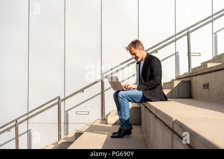 Businessman sitting on steps outdoors using laptop Stock Photo
