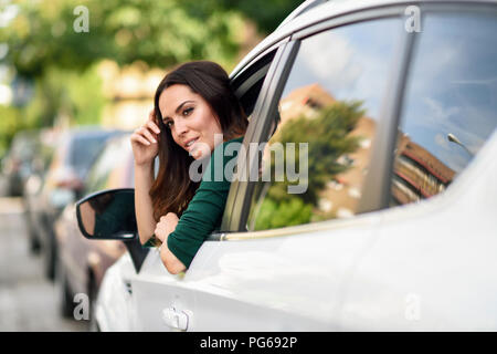 Young woman leaning out the window of her car in the city Stock Photo