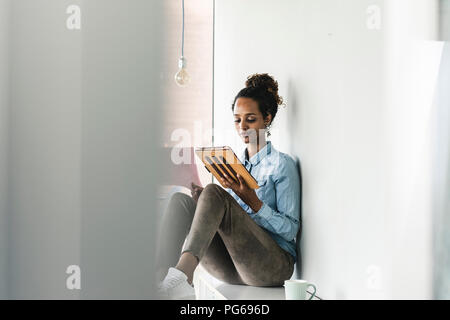 Young businesswoman sitting on shelf, using digital tablet Stock Photo