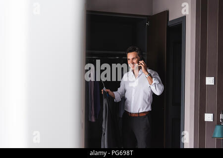 Smiling businessman on cell phone at home getting dressed Stock Photo