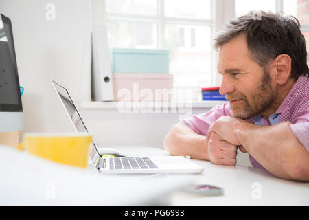 Smiling man leaning on desk in office using tablet Stock Photo