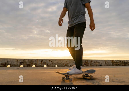 Young Chinese man skateboarding at sunsrise near the beach Stock Photo