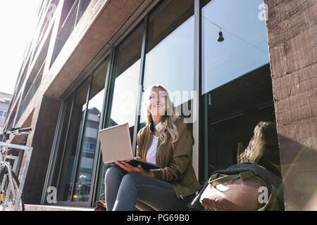 Friends sitting in front of window in the city, using laptop Stock Photo