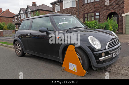 Orange DVLA clamp, immobilising a black mini vehicle, where UK car tax has not been paid, Grappenhall, Warrington, Cheshire, North West England, UK Stock Photo