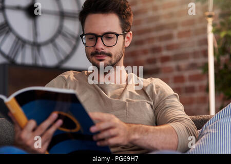 Portrait of man sitting on couch at home reading a book Stock Photo