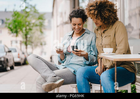 Two friends working in coworking space, sitting at table with coffee, using smartphone Stock Photo