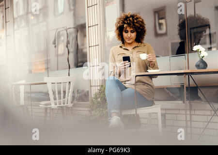 Woman in front of coffee shop, drinking coffee, holding smart phone Stock Photo