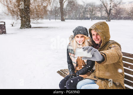 Happy young couple taking selfie with cell phone on snowy day in the park Stock Photo