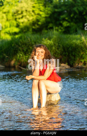 Young woman sitting on stone, river Stock Photo