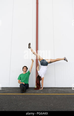 Man spotting woman, doing a one-armed handstand Stock Photo