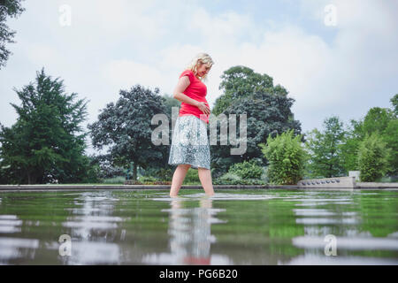 Pregnant woman walking through pond in park Stock Photo