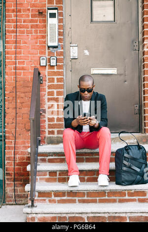 USA, NYC, Brooklyn, Man waiting on stairs, using smartphone Stock Photo