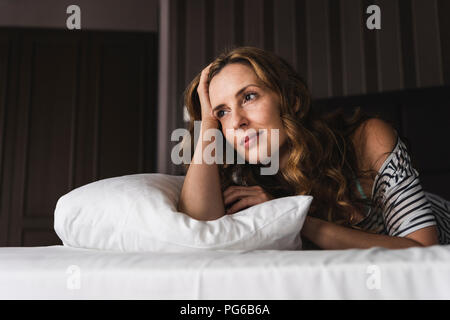 Thoughtful woman lying on bed at home looking away Stock Photo