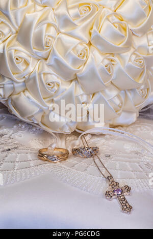 Bride's satin ribbon bouquet on ring bearer's pillow with wedding rings and silver cross with purple stone Stock Photo