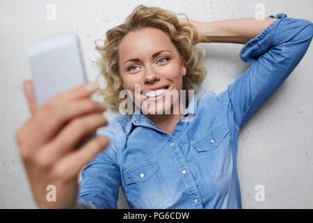 Portrait of smiling blond woman taking selfie with smartphone Stock Photo