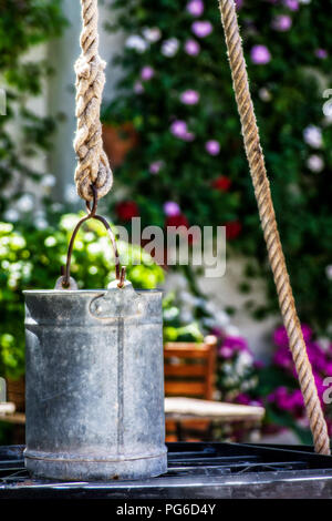 Brass bucket fastened with a rope in a typical Cordovan patio with blurred flowers in the background. Stock Photo