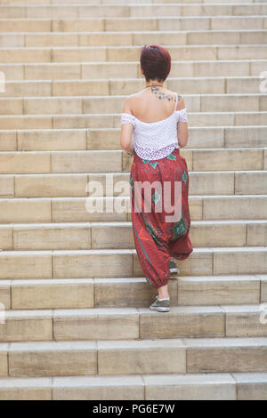 Rear view of a young woman wearing harem pants walking up the stairs outdoors Stock Photo