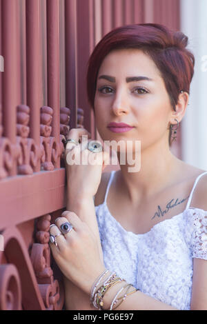 Beautiful young woman with short red hair leaning against a gate outdoors Stock Photo