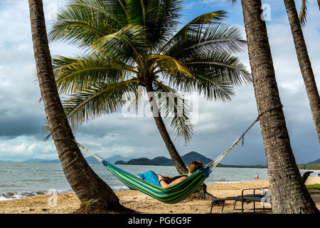 Woman laying in hammock overlooking palm trees and beach Stock Photo