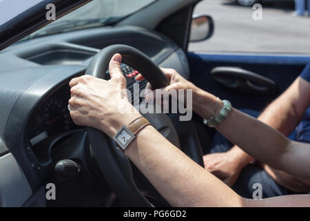 A woman, hands on the steering wheel, learning to drive car at driving school, an instructor by her side Stock Photo