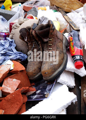 Pair of old workers boots thrown into a builders skip thats almost full outside a building site Stock Photo