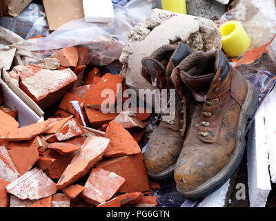 Pair of old workers boots thrown into a builders skip thats almost full outside a building site Stock Photo