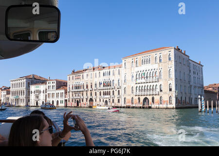 Woman tourist travelling on a vaporetto,  Grand Canal, Venice, Veneto, Italy photographing Ca' Foscari University on a smartphone, First person point  Stock Photo