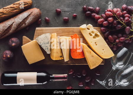 flat lay with baguettes, assorted cheese, bottle of wine and fruits on dark tabletop Stock Photo