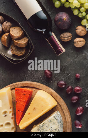 food composition with bottle of wine, grape, bread pieces and assorted cheese on dark surface Stock Photo