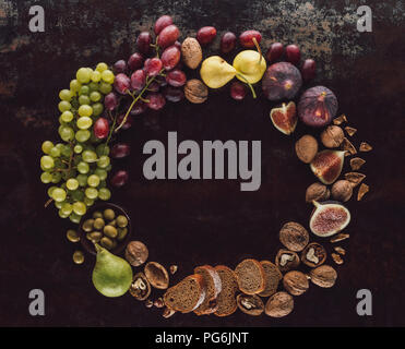 flat lay with various fruits, bread pieces and hazelnuts assorted in circle on dark tabletop Stock Photo