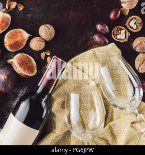 top view of bottle of wine, empty glasses, hazelnuts and figs on dark tabletop Stock Photo