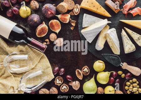 flat lay with assorted cheese, bottle of wine, empty glasses and fruits on dark surface Stock Photo