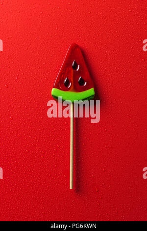 top view of lollipop in shape of watermelon on red surface with water drops Stock Photo