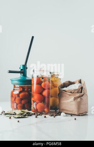 glass jars and tool for preserving tomatoes on table in kitchen Stock Photo