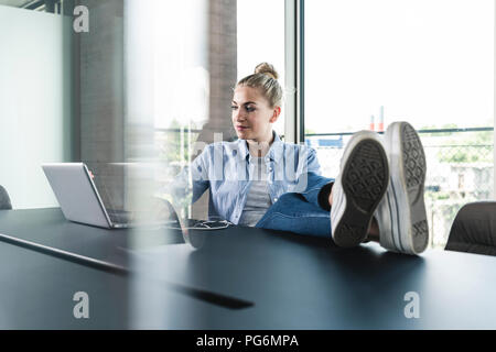 Young businesswoman sitting at desk with feet up, using laptop Stock Photo